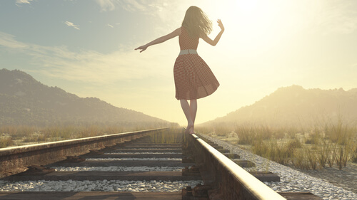 A woman is balancing on railroad tracks.