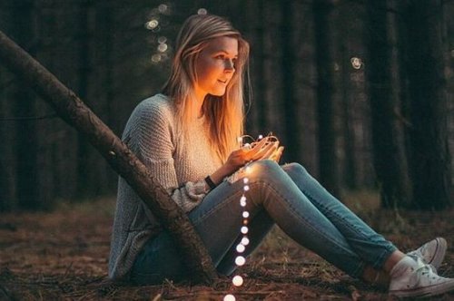 A girl sitting in the woods with string lights.