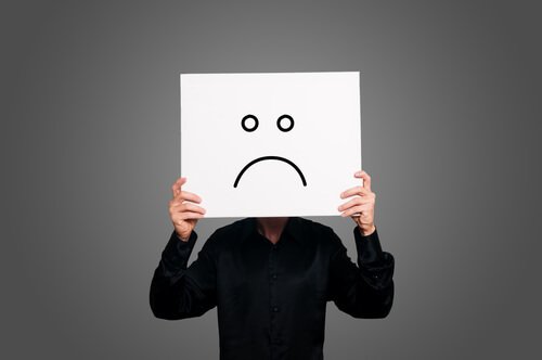 A man has a sad smiley sign covering his face.