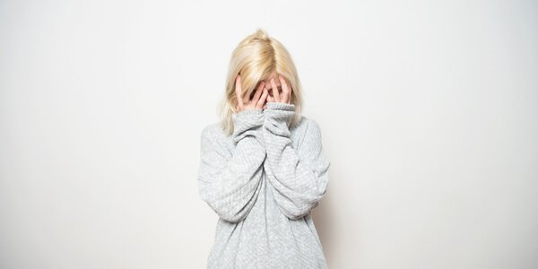 A scared girl that is covering her face.