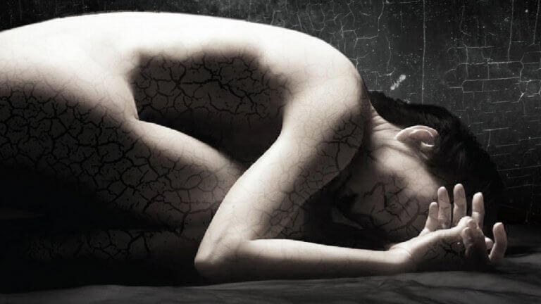en kvinne med fragmentert hud krøllet sammen på bakken