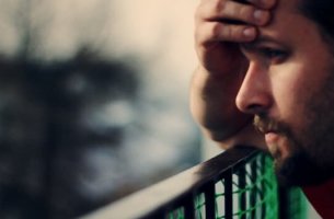 A worried man has his hand on his forehead.