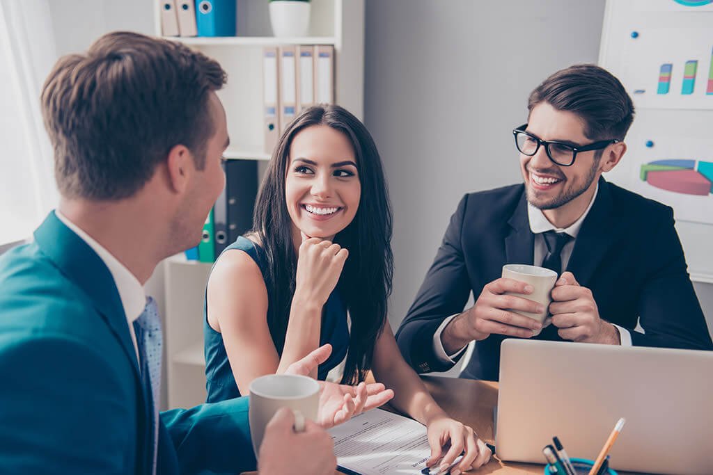 Coworkers smiling and working with coffee at a desk.
