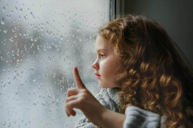 A girl is looking out a window on a rainy day.