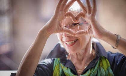 An older woman making a heart with her hands.