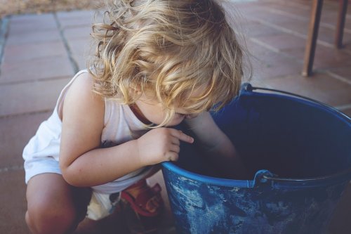 A little girl is reaching into a bucket.