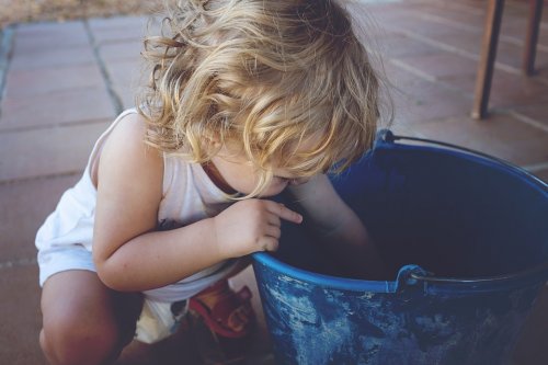 A little girl is reaching into a bucket. 