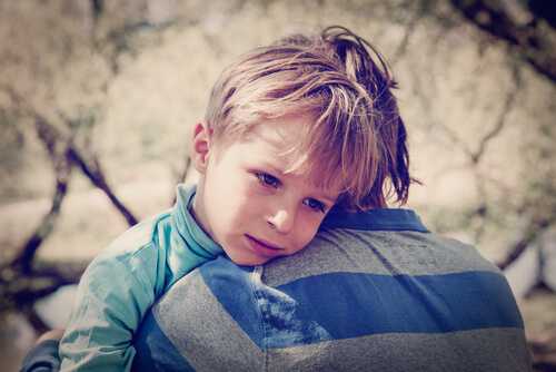 A sad boy is being hugged by an adult.