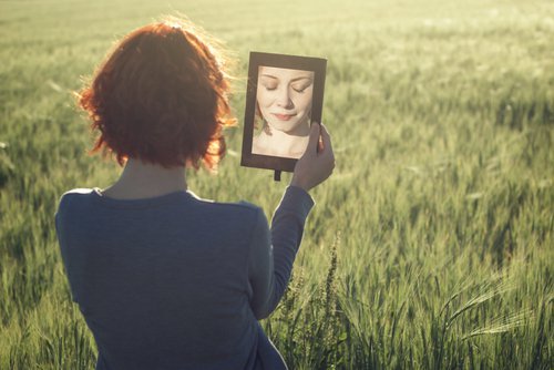 Woman in a field looking in a mirror.