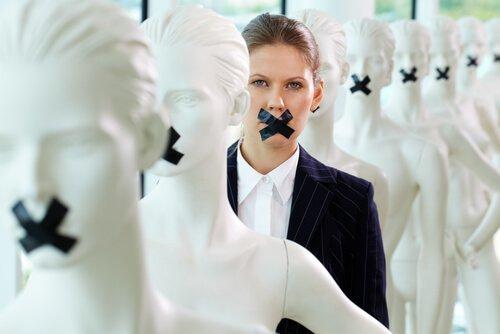 A woman silenced with tape over her mouth along with mannequins.