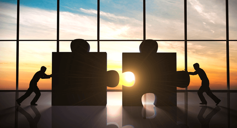 Two figures pushing together two giant puzzle pieces.