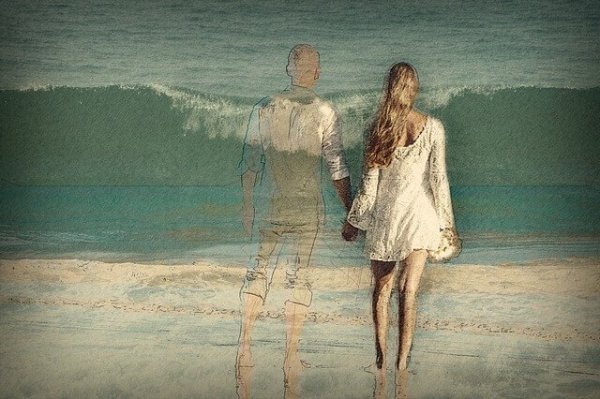 A couple on the beach, the man transparent like a ghost.