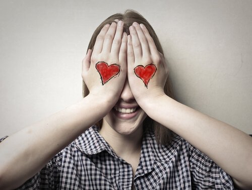 woman covering her eyes with her hands (which have hearts on them) symbolizing blind love