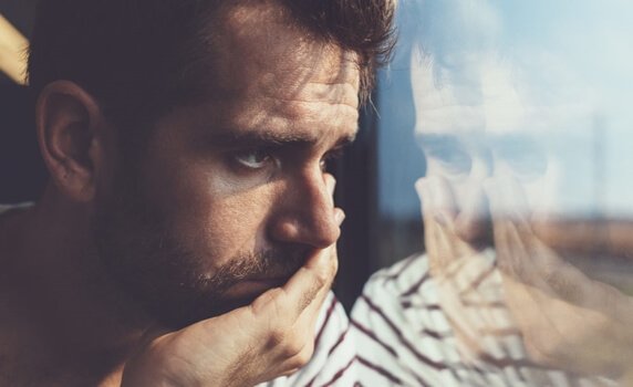 sad man going through the stages of grief looking out the window