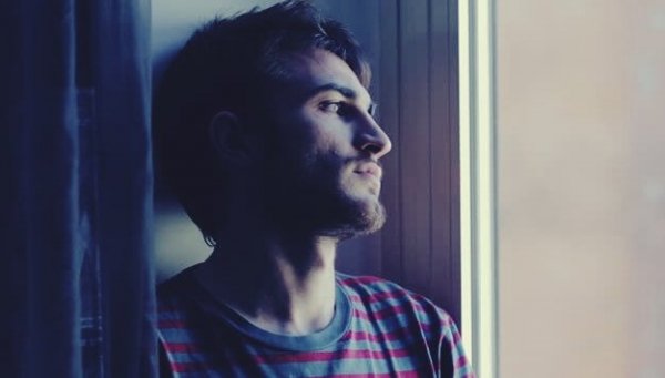 A sad 30-year-old man looking out the window.