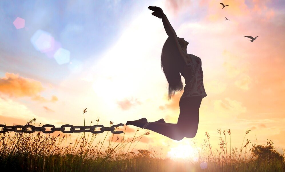 The silhouette of a woman jumping in the air and breaking herself free of chains.