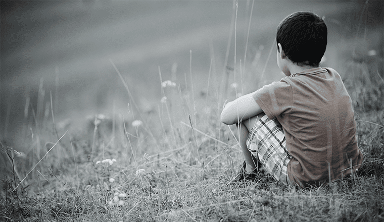 A traumatized child sitting in a field.
