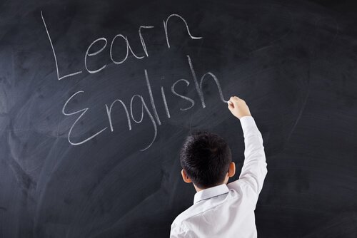 Boy writing in English on a chalkboard.