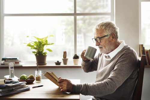 Elderly man reading while drinking coffee.