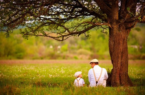 Father and son talking under a tree.