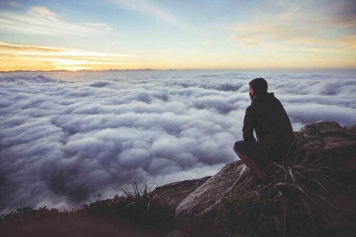 Man on a mountain looking down to a sea of clouds.