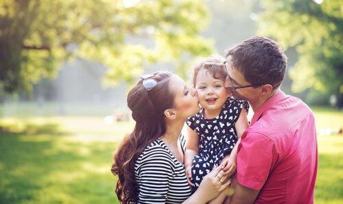 Parents hugging their daughter in a field.