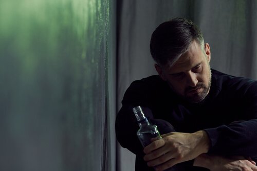 A sad man holding a bottle of alcohol.