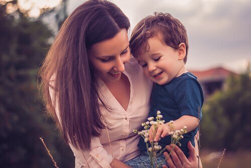 A woman holding her son in her arms while picking up flowers.