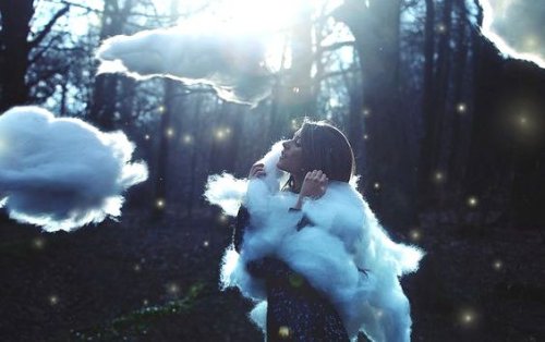 Woman in a forest, surrounded by clouds.