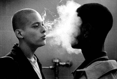 A white guy blowing smoke in a black guy's face.