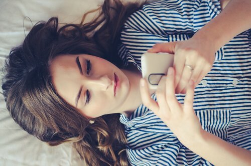 Girl lies in bed with phone.