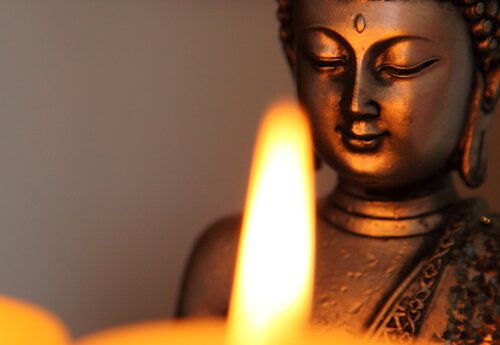 A Buddha statue in front of a candle flame.