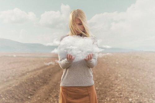 A blonde woman standing in a barren field holding a small cloud.