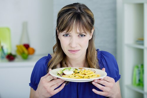 A woman holding a plate of pasta and looking disgusted.