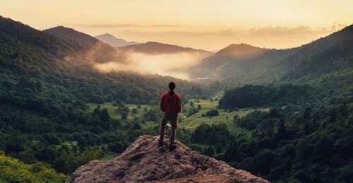 A man observing the landscape from the top of a mountain.
