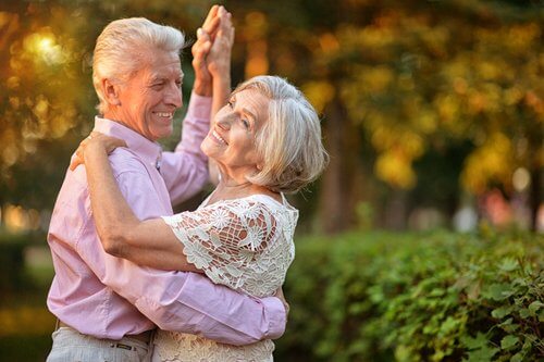 An older man and woman dancing together with smiles on their faces.