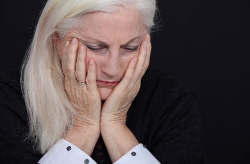 A close-up of an older woman holding her face in her hands.