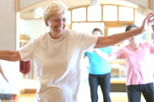 An older woman dancing with a smile on her face.