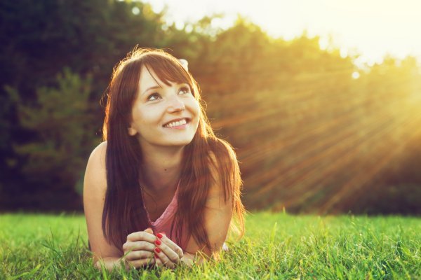 A woman smiling and looking up at the sun.
