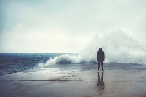 A guy watching a wave break on a pier.