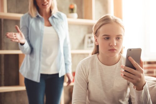 Girl looking at a cell phone, with a frustrated adult behind her.