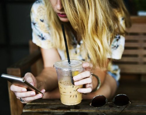 A woman on her phone while drinking iced coffee.