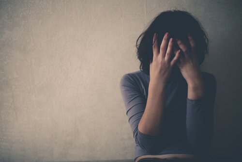 A depressed woman covering her face in front of a wall.