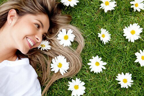 Kobieta leżąca obok kwiatów i uśmiechnięta.