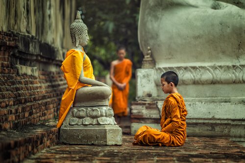 A boy sitting front of a statue of Buddha.