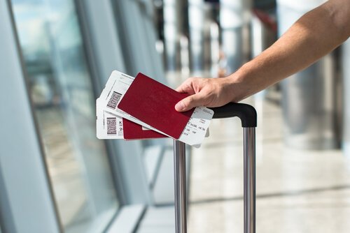 A person walking through an airport with their suitcase and two passports in hand.