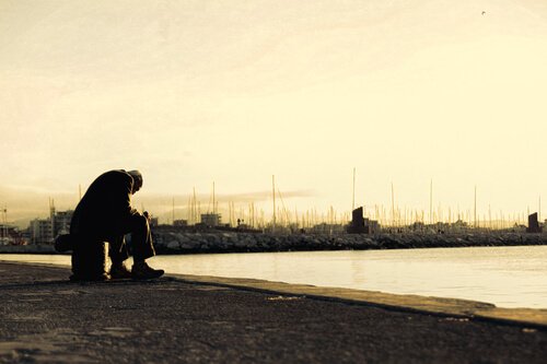 A sad old man sitting by himself in front of a lake.