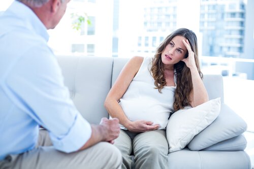 A stressed pregnant woman sitting on the couch.
