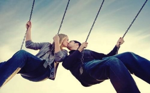 A couple kissing on some swings.