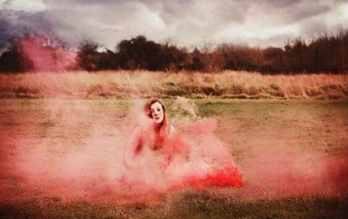 A woman in a field surrounded by pink smoke.